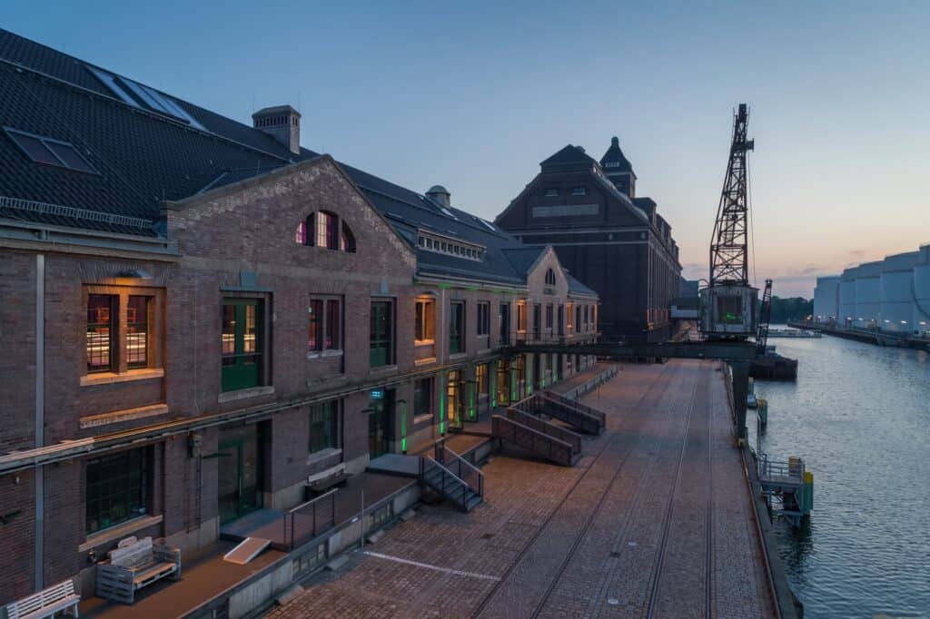 Angrenzend an das Wasser ist das Fabrikgebäude des WECC Event & Covention Centers in bezauberndes Abendlicht getaucht.