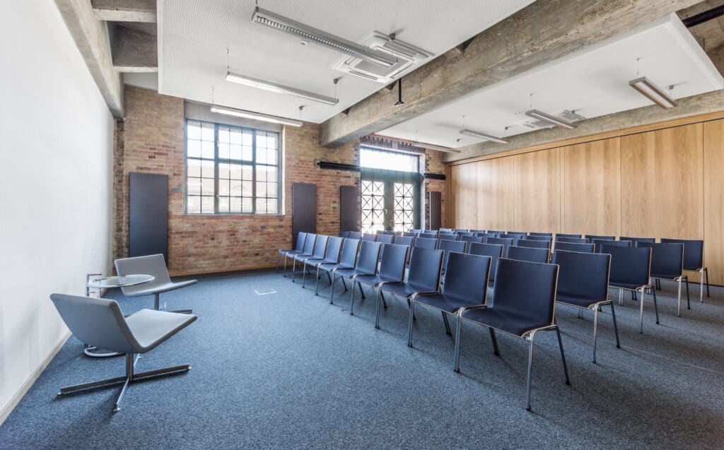Ein weitläufiger Raum, geschmückt mit bequemen Stühlen und einem auffälligen Projektor, bietet einen gut ausgestatteten Platz für Konferenzen oder Vorlesungen.